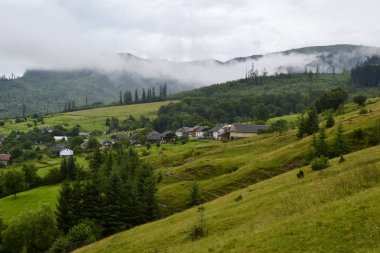 Bir vadide köyün çarpıcı görünümü. Dağ sırasının üzerindeki bulutlar. Karpat dağları, Ukrayna