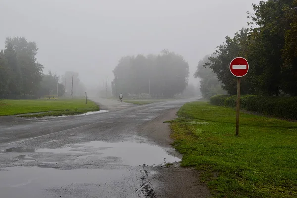 Fork in the road with puddles after the rain. Empty landscape with no entry sign on a foreground. Foggy rainy weather.