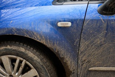 Mavi arabanın yan tarafına çamur sıçradı. Yolda yağmurlu havalarda kirli araç.