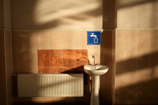 Beyaz lavabo, Ukrayna, Pomichna 'da, demiryolu istasyonunun bekleme salonunda, duvarın yanında mavi musluk işareti. Kontrast sabah ışığı ve gölgeler