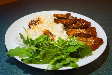 Kızarmış soya eti domates sosu ve haşlanmış pirinç ile baharat haşlanmış. Taze yeşil arugula yaprakları ile beyaz tabakta servis edilir. Yakından kapatın. Seçici odaklama.