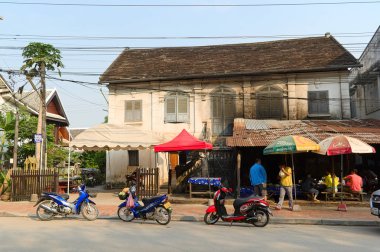 Luang Prabang, Laos - Nisan, 2015: Park halindeki motosikletli küçük kafe. Eski sömürge binaları.