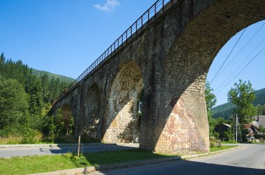 Vorokhta, Ukrayna - Ağustos, 2019: Yol üzerinde eski kemer demiryolu köprüsü. Kemerden birinde Hutsul'un sokak sanatı resmi. Vorokhta, Karpat dağları, Ukrayna.