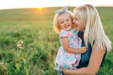 Hapy anne ile küçük kızı alanında günbatımında eğleniyor. Kadın kız ile gülüyor.