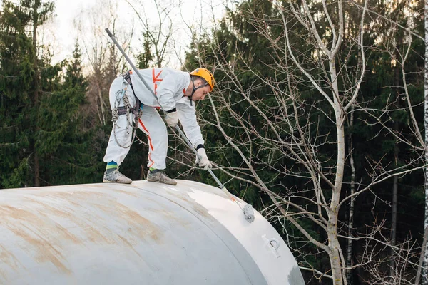 Industrial climber in helmet and uniform painting water tower. Professional Painter working on height. Risky job. Extreme occupation.