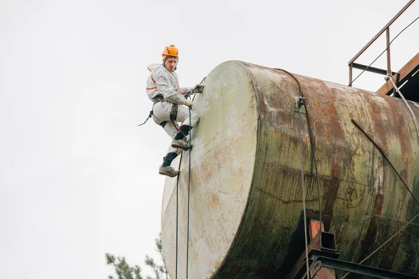 Industrial climber in uniform and helmet working on height outdoors. Professional worker doing his risky job on water tower.