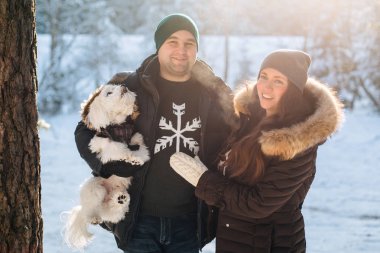 Sevimli Genç çift ile onların küçük beyaz köpek kış ormandaki eğleniyor. Erkek ve kadın kazaklı bir kar tanesi ile