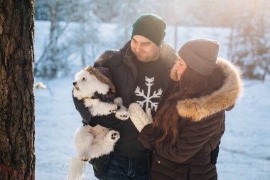 Sevimli Genç çift ile onların küçük beyaz köpek kış ormandaki eğleniyor. Erkek ve kadın kazaklı bir kar tanesi ile