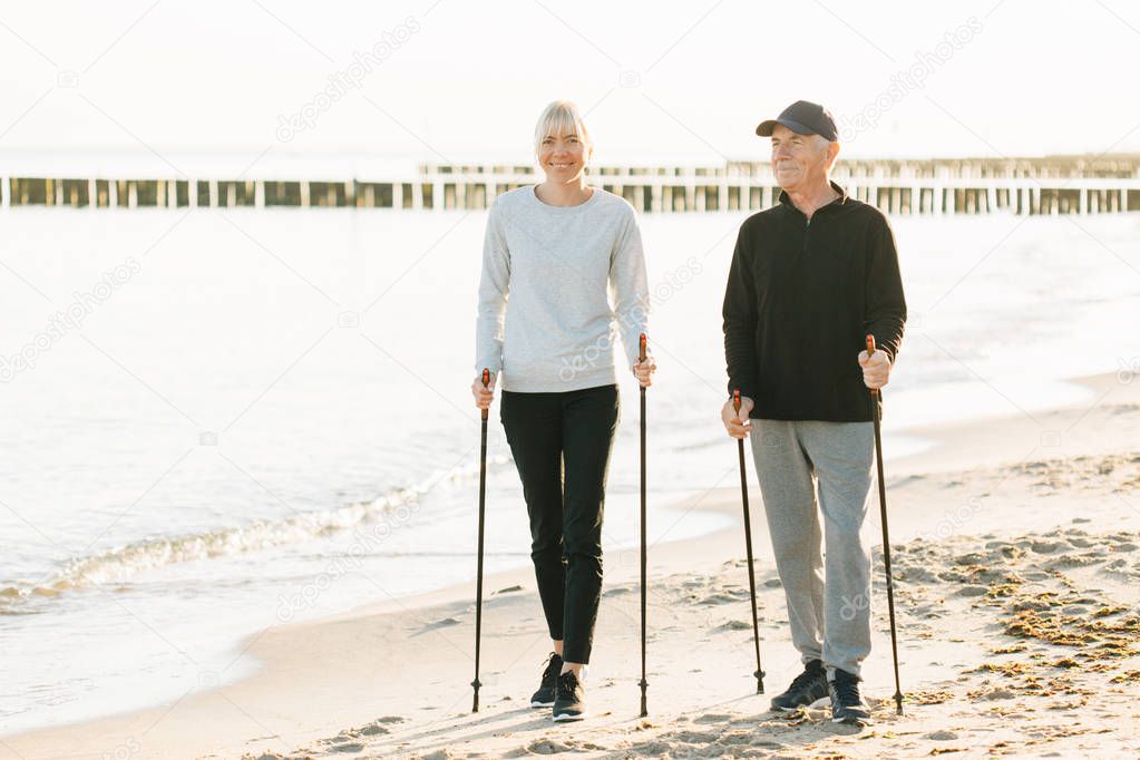 Nordic walking - senior man and pretty young girl working out on beach. Healthy lifestyle. Candid photo of father and daughter.