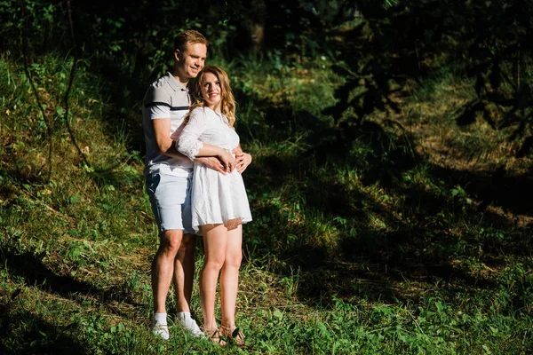 恋爱中的年轻夫妇站在公园里 英俊的金发女孩在白色礼服拥抱她的男朋友 — 图库照片