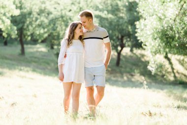 Genç ve güzel bir çift parkta yürüyor. Beyaz elbiseli, yakışıklı, sarışın kız erkek arkadaşına sarılıyor. Erkek ve kadın dışarıda eğleniyor.