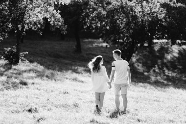 Parkta yürüyen aşık genç güzel çiftin arka görünümü. Onun erkek arkadaşı sarılma beyaz elbiseli yakışıklı neşeli sarışın kız. Dışarıda eğlenen kadın ve erkek