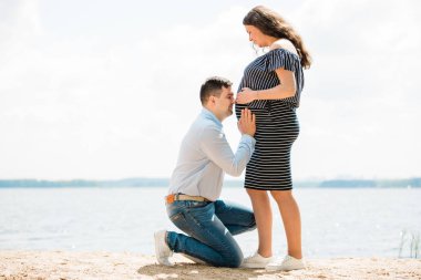 Yakışıklı adam hamile karısının karnını dinliyor. Karnına yakın bir geleceğin babası. Mutlu gebelik kavramı.