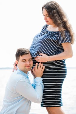 Yakışıklı adam hamile karısının karnını dinliyor. Karnına yakın bir geleceğin babası. Mutlu gebelik kavramı.