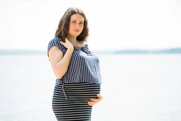 Cheerful pregnant woman with long hair standing on the beach. Happy pregnancy concept.