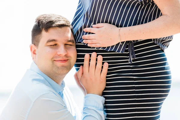 Yakışıklı adamın portre çekim hamile karısının karnını dinliyor. Karnına yakın bir geleceğin babası. Mutlu gebelik kavramı.