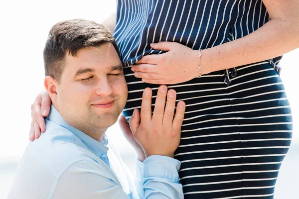 Yakışıklı adamın portre çekim hamile karısının karnını dinliyor. Karnına yakın bir geleceğin babası. Mutlu gebelik kavramı.