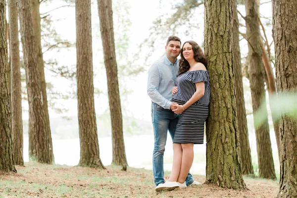 愉快的孕妇长头发站在森林里与她的丈夫 正在生孩子的年轻家庭 快乐怀孕的概念 — 图库照片