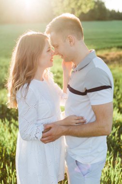 Genç çift aşk ayakta parkta güzel. Beyaz elbiseli erkek arkadaşıyla sarılma yakışıklı neşeli sarışın kız. Erkek ve kadın dışarıda eğleniyor