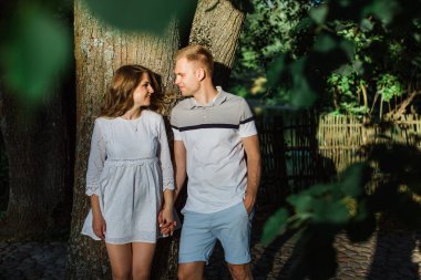 Genç çift aşk ayakta parkta güzel. Beyaz elbiseli erkek arkadaşıyla sarılma yakışıklı neşeli sarışın kız. Erkek ve kadın dışarıda eğleniyor