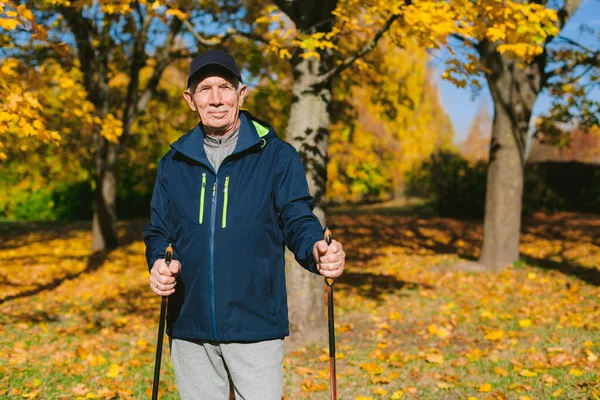 Lächelnder Alter Mann Der Sich Nach Dem Nordic Walking Herbstpark lizenzfreie Stockbilder