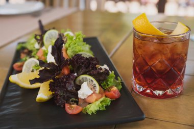 kafenin arka planında peynir, domates, narenciye, fesleğen ve marul ve soda ve buz ile kokteyl salatası