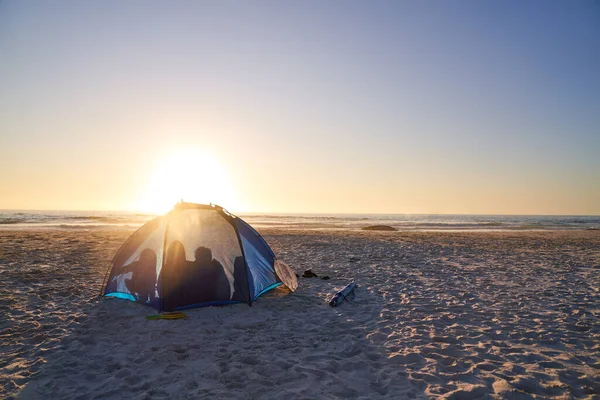 日落时分在阳光明媚的海滩上的帐篷里 一家人的轮廓 — 图库照片