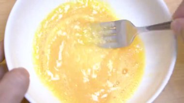 Eller beat yumurta sabah kahvaltıda omlet hazırlamak için beyaz bir kase içinde yakın çekim.
