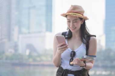 Güzel Asya gülümseyerek ve spot gezi turist aramak için cep telefonu bakarak turist kadın solo. Yaz aylarında tatil seyahat.