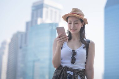 Güzel Asya gülümseyerek ve spot gezi turist aramak için cep telefonu bakarak turist kadın solo. Yaz aylarında tatil seyahat