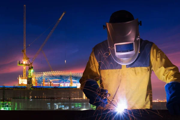 Industriearbeiter schweißt Stahlkonstruktion für Infrastrukturbauprojekt mit Baustelle im Hintergrund. — Stockfoto