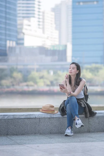 Hermosa mujer turista asiática sola relajándose y disfrutando escuchando la música en un teléfono inteligente en el centro urbano de la ciudad — Foto de Stock