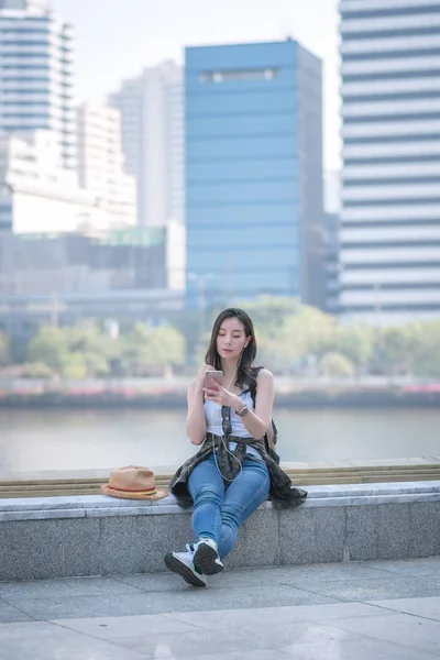 Piękna Azjatycka kobieta turystyczna relaksująca i ciesząca się słuchając muzyki na smartfonie w miejskim centrum miasta — Zdjęcie stockowe