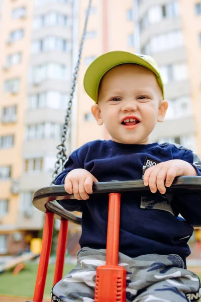 Engraçado e bonito menino se alegra, passeios em um balanço de crianças, joga no parque infantil . — Fotografia de Stock