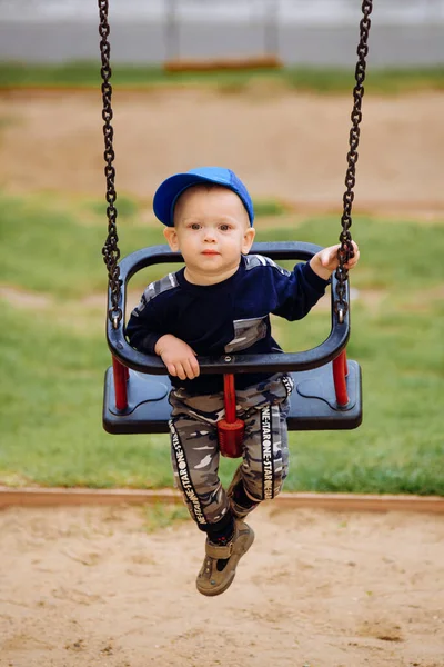 Engraçado e bonito menino se alegra, passeios em um balanço de crianças, joga no parque infantil, 1-2 anos — Fotografia de Stock