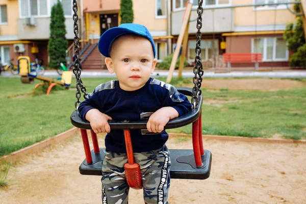 Engraçado e bonito menino se alegra, passeios em um balanço de crianças, joga no parque infantil — Fotografia de Stock