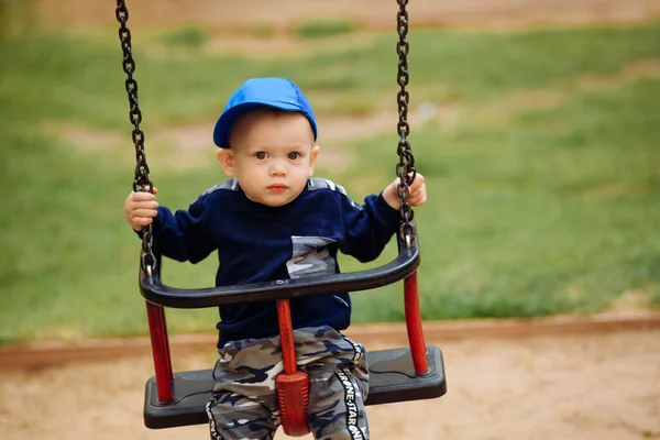 Engraçado e bonito menino se alegra, passeios em um balanço de crianças, joga no parque infantil, 1-2 anos — Fotografia de Stock