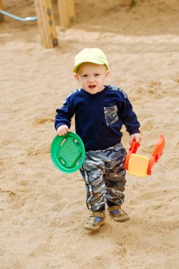 1-2 yaşındaki neşeli bir çocuk oyun parkında oyuncaklarla oynuyor.