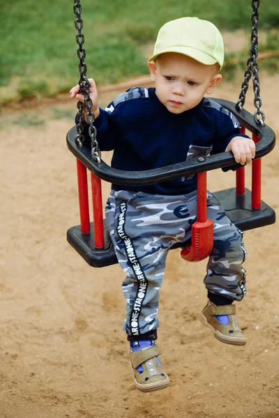 O menino senta-se em um balanço, parece surpreso, 1-2 anos — Fotografia de Stock