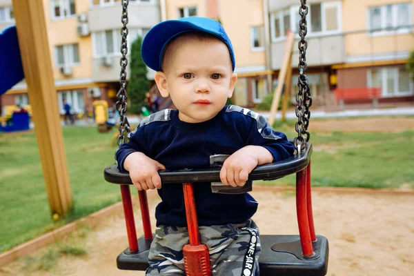 Engraçado e bonito menino se alegra, passeios em um balanço de crianças, joga no parque infantil — Fotografia de Stock