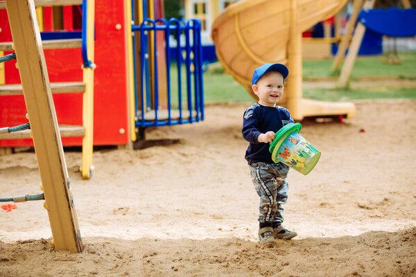Playground, cheerful boy smiles and plays with toys, 1-2 years old