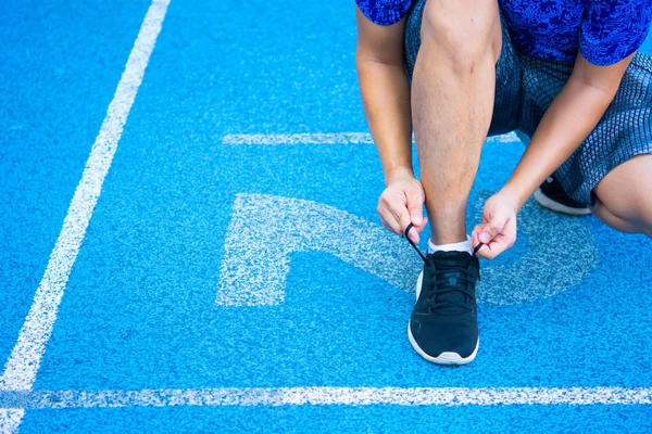 Sport man in blue t-shirt with shorts is wearing black sport shoes on synthetic blue floor with white lane