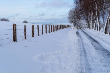 Bir kış manzarası, dikenli tel çit yol boyunca aracılığıyla karlı yol