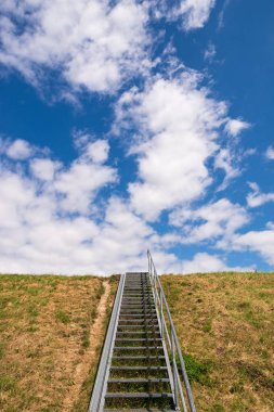 Bir dike, sarı çim en üstüne metal merdiven ve beyaz bulutlar ile mavi gökyüzü, Aşağı Saksonya, Almanya