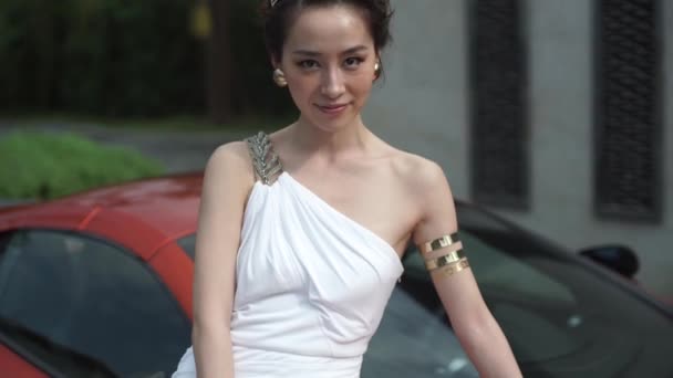 Attractive chinese girl in beautiful white dress stands near the modern sportcar — Stock Video