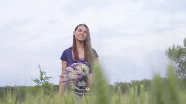 Joven chica sube la colina y recoge un ramo de flores silvestres — Vídeos de Stock