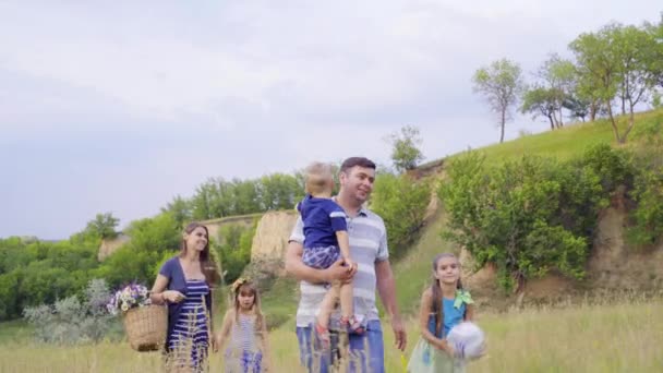 Jovem família feliz com três crianças indo para piquenique em colinas verdes. 4K — Vídeo de Stock