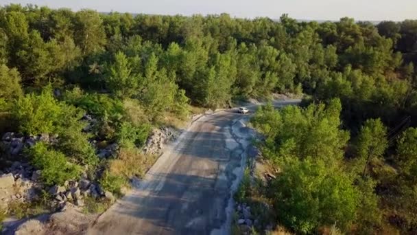 La voiture va sur un chemin de terre entre les arbres et les collines. 4k 