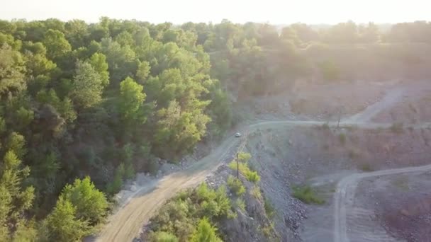 O carro está indo em uma estrada de terra entre árvores e colinas. 4k — Vídeo de Stock