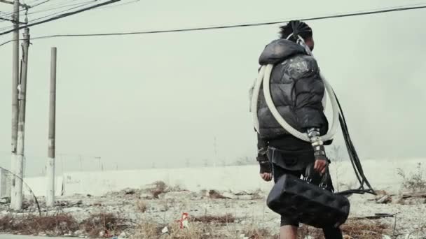 Постапокалипсис, одинокая молодая женщина гуляет среди свалки мусора и заброшенного города — стоковое видео